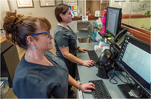 Jessica Carlson, COT, and Andrea O'Leary, COT, consult patient charts in a tech station.