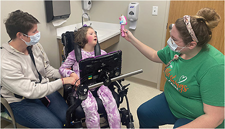 Ophthalmic technician using a toy to check fixation in a child with multiple disabilities while Mom is calming the patient with a supportive gentle touch.IMAGE COURTESY DR. RICHARD W. HERTLE